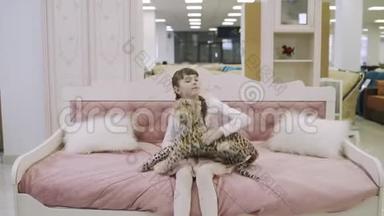 漂亮的少女坐在家具店的粉红色儿童床上。 在购物中心挑选家具的年轻女孩